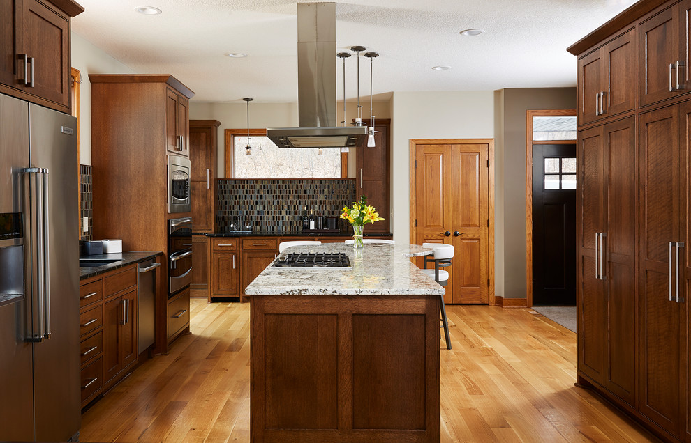 Inspiration for a transitional u-shaped medium tone wood floor and brown floor kitchen remodel in Minneapolis with an undermount sink, shaker cabinets, medium tone wood cabinets, multicolored backsplash, mosaic tile backsplash, stainless steel appliances, an island and white countertops