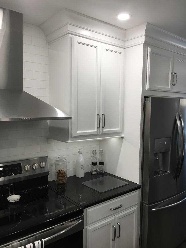 Exempel på ett stort modernt svart svart kök, med en undermonterad diskho, skåp i shakerstil, vita skåp, granitbänkskiva, vitt stänkskydd, stänkskydd i keramik, rostfria vitvaror, laminatgolv, en köksö och brunt golv