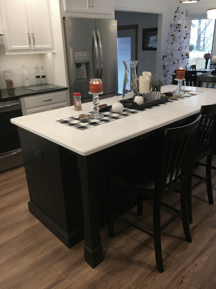 This is an example of a large modern l-shaped kitchen/diner in Other with a submerged sink, shaker cabinets, white cabinets, granite worktops, white splashback, ceramic splashback, stainless steel appliances, laminate floors, an island, brown floors and black worktops.