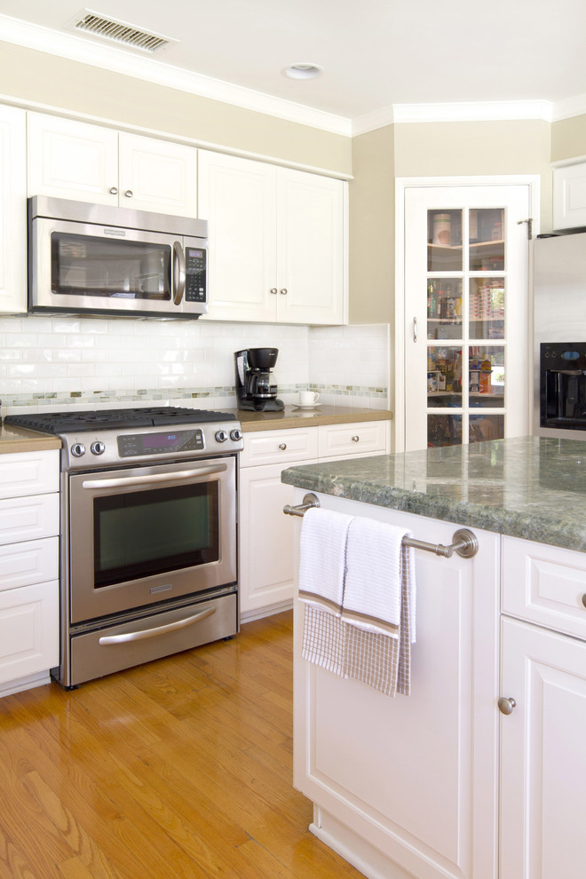 Klassisk inredning av ett mellanstort kök, med luckor med upphöjd panel, vita skåp, marmorbänkskiva, vitt stänkskydd, stänkskydd i tunnelbanekakel, rostfria vitvaror, mellanmörkt trägolv och en köksö