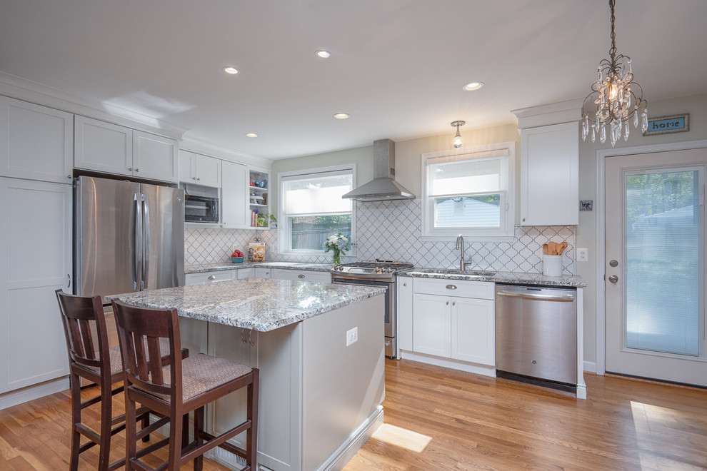 Photo of a medium sized classic l-shaped open plan kitchen in DC Metro with a submerged sink, shaker cabinets, white cabinets, granite worktops, white splashback, ceramic splashback, stainless steel appliances, medium hardwood flooring, an island, brown floors and grey worktops.