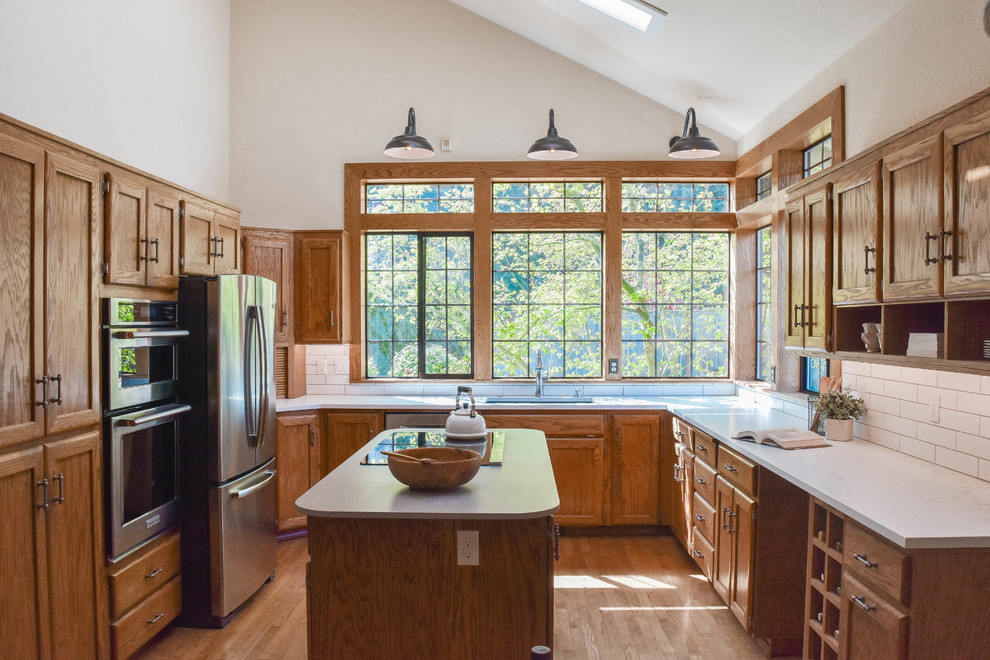 Elegant u-shaped medium tone wood floor and brown floor kitchen photo in Seattle with an undermount sink, recessed-panel cabinets, medium tone wood cabinets, white backsplash, subway tile backsplash, stainless steel appliances, an island and white countertops