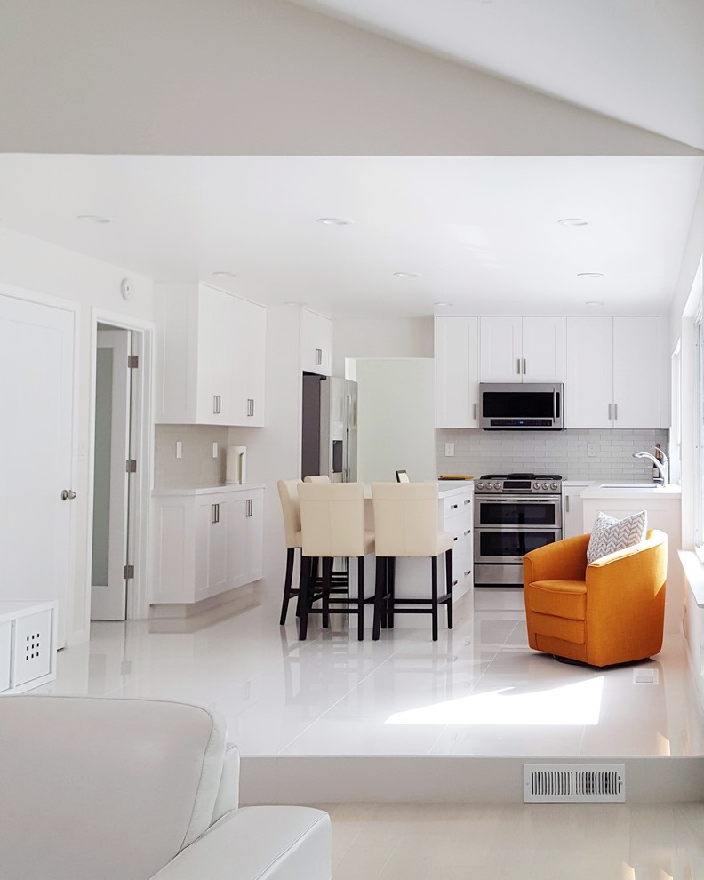Bild på ett funkis vit vitt kök, med en undermonterad diskho, skåp i shakerstil, vita skåp, bänkskiva i kvarts, vitt stänkskydd, glaspanel som stänkskydd, rostfria vitvaror, klinkergolv i porslin, en köksö och vitt golv
