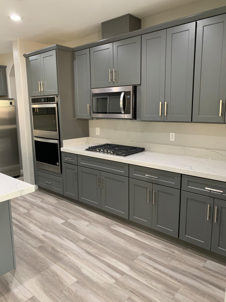 Example of a large trendy laminate floor and gray floor eat-in kitchen design in Las Vegas with an undermount sink, shaker cabinets, gray cabinets, quartzite countertops, stainless steel appliances, an island and white countertops