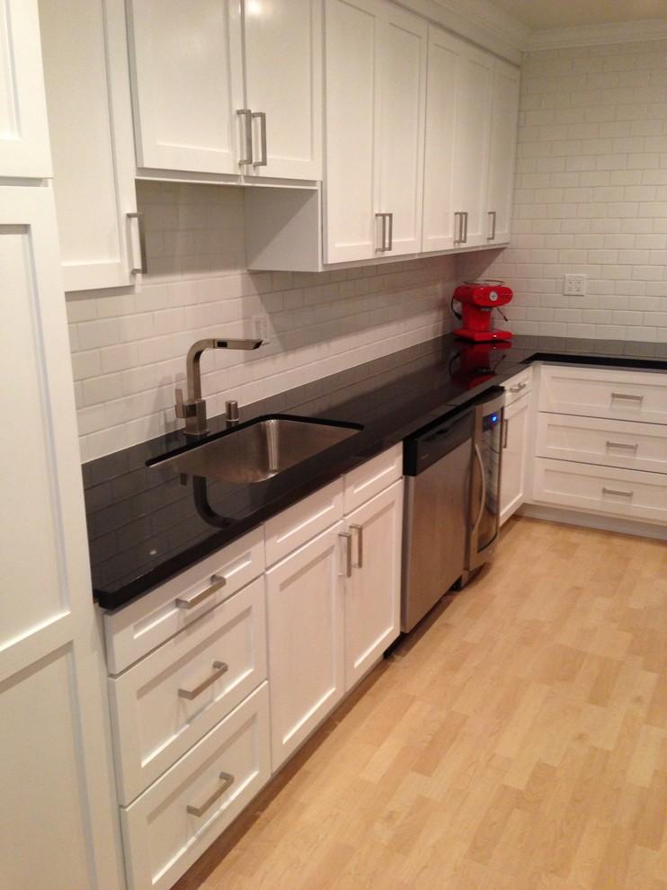 Photo of a small classic galley enclosed kitchen in Los Angeles with a submerged sink, recessed-panel cabinets, white cabinets, composite countertops, white splashback, metro tiled splashback, stainless steel appliances, light hardwood flooring and no island.