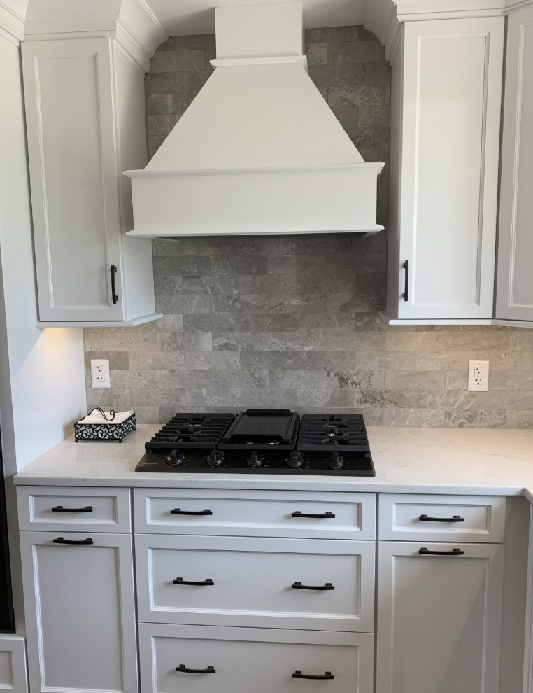 Klassisk inredning av ett stort vit vitt kök, med en undermonterad diskho, luckor med infälld panel, vita skåp, bänkskiva i kvarts, grått stänkskydd, stänkskydd i keramik, rostfria vitvaror, vinylgolv, en köksö och grått golv