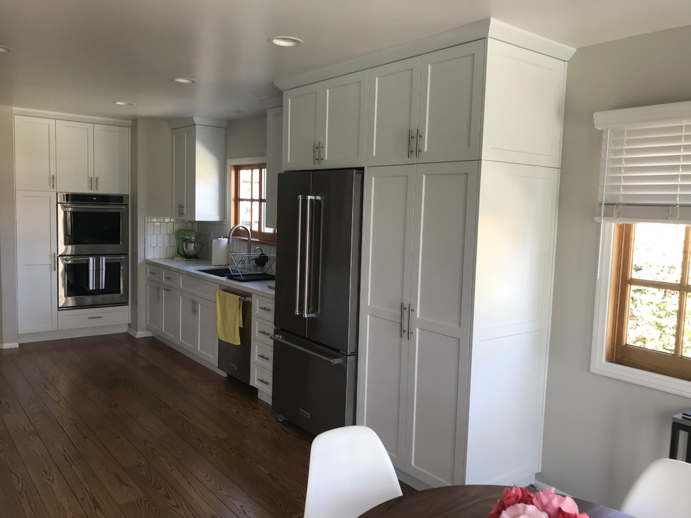 Classic u-shaped kitchen/diner in Portland with a submerged sink, shaker cabinets, white cabinets, white splashback, metro tiled splashback, stainless steel appliances, dark hardwood flooring, no island, brown floors, white worktops and engineered stone countertops.