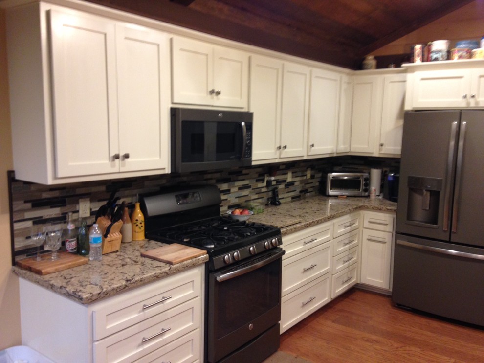 Example of a mid-sized classic l-shaped medium tone wood floor and brown floor enclosed kitchen design in Los Angeles with shaker cabinets, white cabinets, granite countertops, multicolored backsplash, matchstick tile backsplash, stainless steel appliances, no island and beige countertops