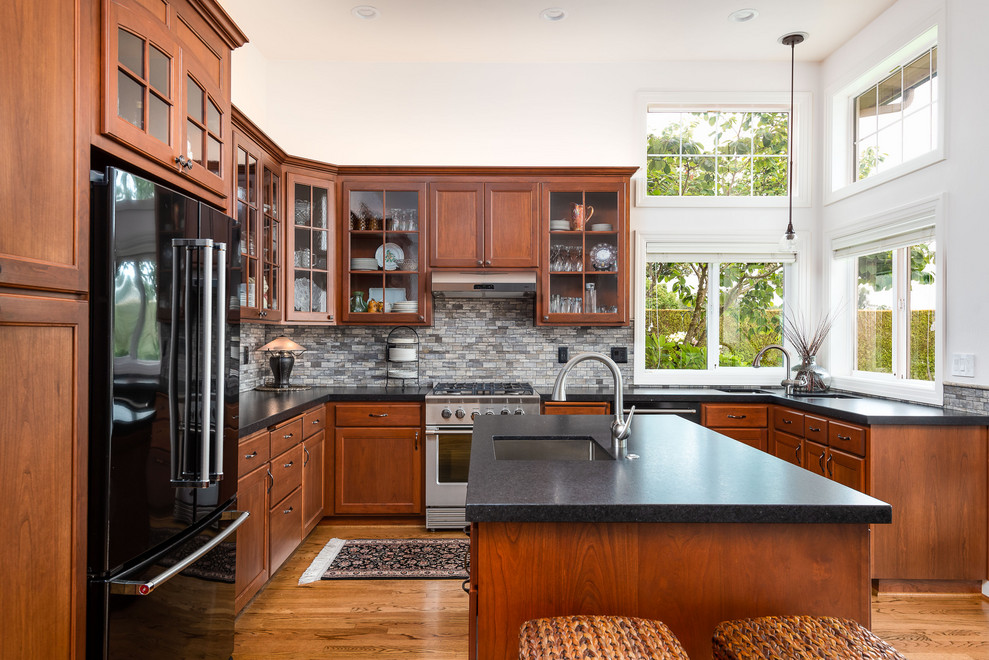 Exempel på ett mellanstort medelhavsstil svart svart kök, med en undermonterad diskho, skåp i shakerstil, skåp i mellenmörkt trä, granitbänkskiva, flerfärgad stänkskydd, stänkskydd i stenkakel, rostfria vitvaror, mellanmörkt trägolv, en köksö och brunt golv