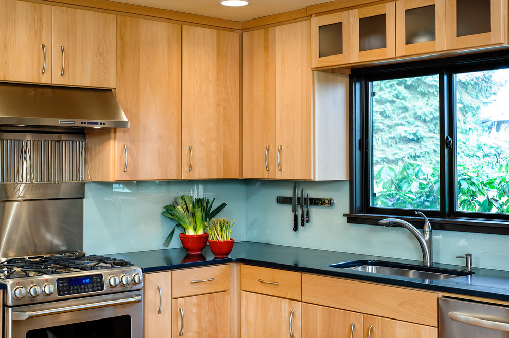 Bild på ett mellanstort funkis kök, med en undermonterad diskho, släta luckor, skåp i ljust trä, bänkskiva i kvarts, glaspanel som stänkskydd, rostfria vitvaror, korkgolv och en köksö