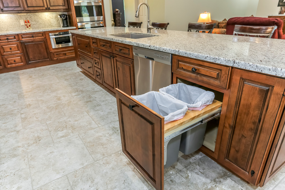 This is an example of a rustic l-shaped open plan kitchen in Houston with raised-panel cabinets, medium wood cabinets, stainless steel appliances, an island, a submerged sink, granite worktops, grey splashback, stone slab splashback and travertine flooring.