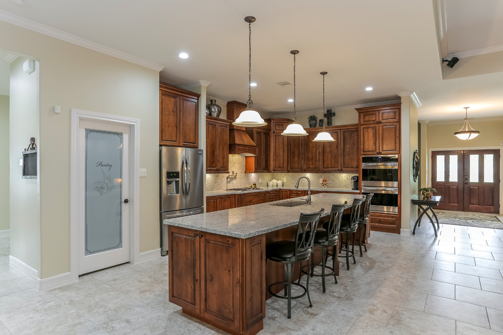 This is an example of an expansive rustic l-shaped open plan kitchen in Houston with raised-panel cabinets, medium wood cabinets, an island, a submerged sink, granite worktops, grey splashback, stone slab splashback, stainless steel appliances and travertine flooring.