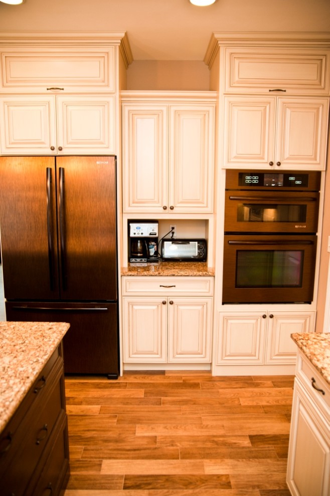 Mid-sized transitional l-shaped dark wood floor eat-in kitchen photo in New York with an undermount sink, raised-panel cabinets, white cabinets, granite countertops, beige backsplash, ceramic backsplash, black appliances and an island