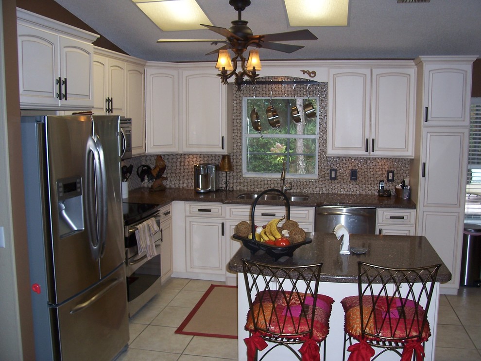 Foto på ett litet funkis kök, med en dubbel diskho, luckor med upphöjd panel, vita skåp, stänkskydd i mosaik, rostfria vitvaror, en köksö, granitbänkskiva, flerfärgad stänkskydd och beiget golv