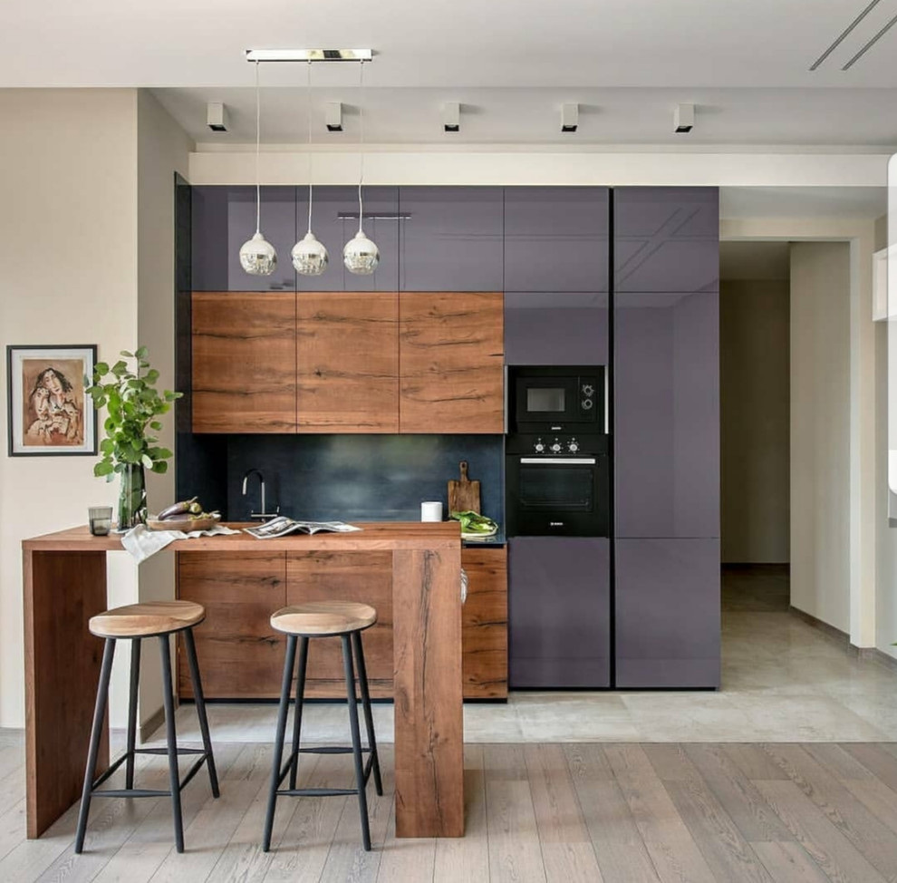 This is an example of a medium sized modern single-wall kitchen/diner in Miami with a submerged sink, flat-panel cabinets, dark wood cabinets, granite worktops, black splashback, stone slab splashback, black appliances, marble flooring, an island, beige floors and black worktops.