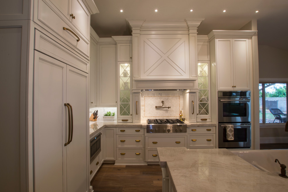 Foto på ett stort lantligt kök, med en rustik diskho, vita skåp, bänkskiva i kvartsit, stänkskydd i stenkakel, rostfria vitvaror, mellanmörkt trägolv, en köksö, luckor med infälld panel och vitt stänkskydd