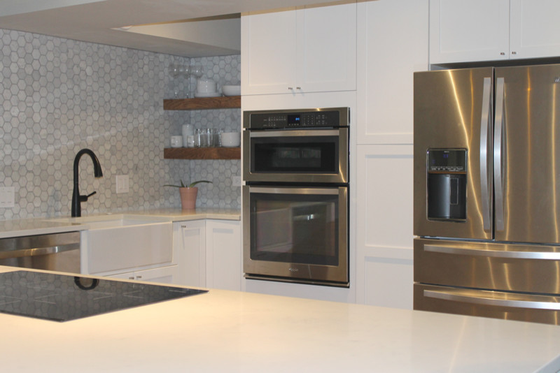 This is an example of a large scandinavian u-shaped kitchen/diner in Chicago with flat-panel cabinets, white cabinets, laminate countertops, white splashback, ceramic splashback, stainless steel appliances, medium hardwood flooring, a belfast sink, a breakfast bar and brown floors.
