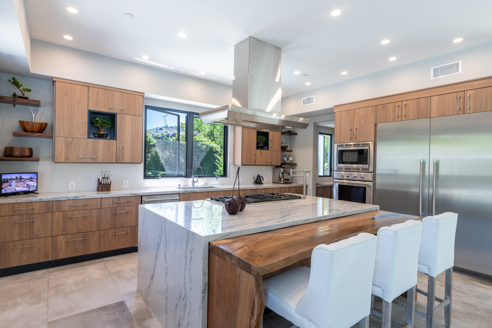 Trendy l-shaped gray floor kitchen photo in Los Angeles with an undermount sink, flat-panel cabinets, medium tone wood cabinets, stainless steel appliances, an island and white countertops
