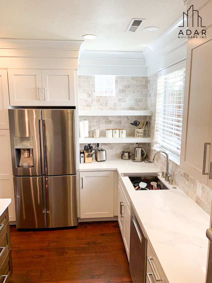 This is an example of a large classic u-shaped open plan kitchen in Los Angeles with recessed-panel cabinets, white cabinets, marble worktops, beige splashback, stone tiled splashback, stainless steel appliances, dark hardwood flooring, an island, brown floors, a submerged sink and white worktops.
