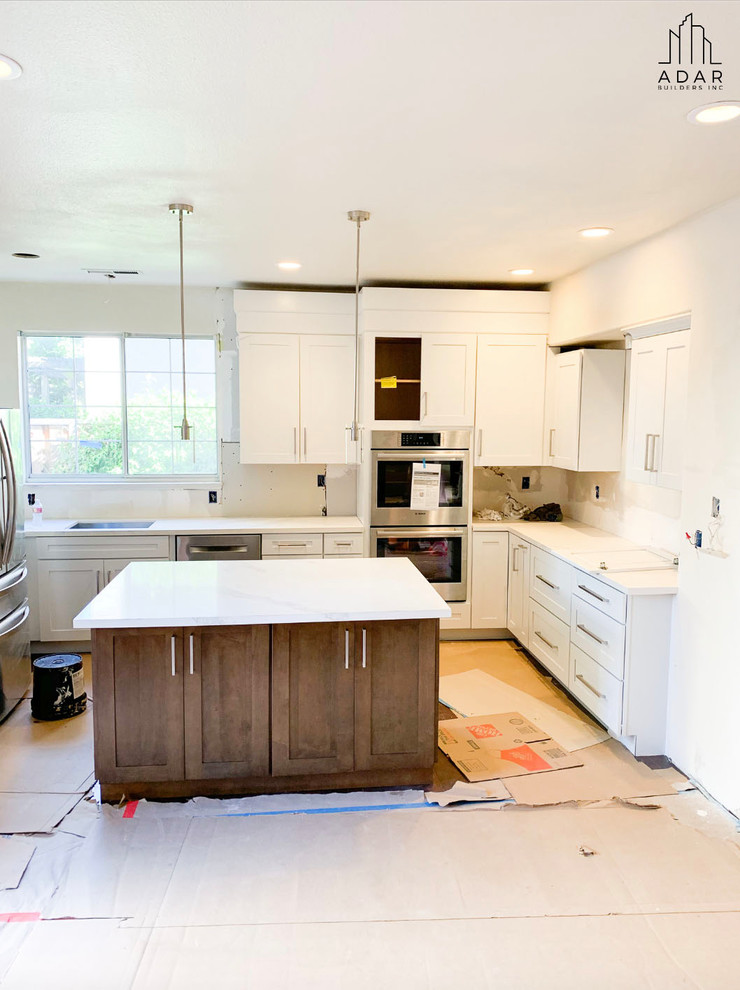 Klassisk inredning av ett stort vit vitt kök, med luckor med infälld panel, vita skåp, marmorbänkskiva, beige stänkskydd, stänkskydd i stenkakel, rostfria vitvaror, mörkt trägolv, en köksö, brunt golv och en undermonterad diskho