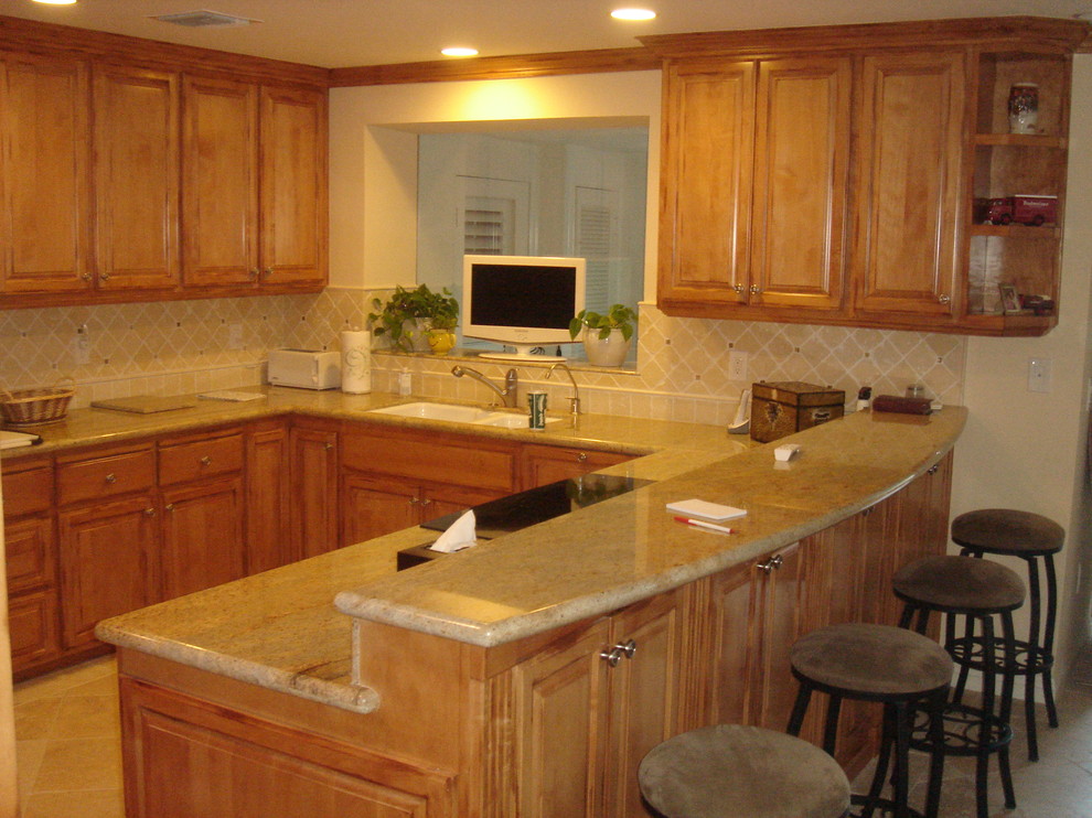 Example of a large classic u-shaped travertine floor eat-in kitchen design in San Diego with an undermount sink, raised-panel cabinets, medium tone wood cabinets, granite countertops, beige backsplash, stone tile backsplash, stainless steel appliances, a peninsula and beige countertops