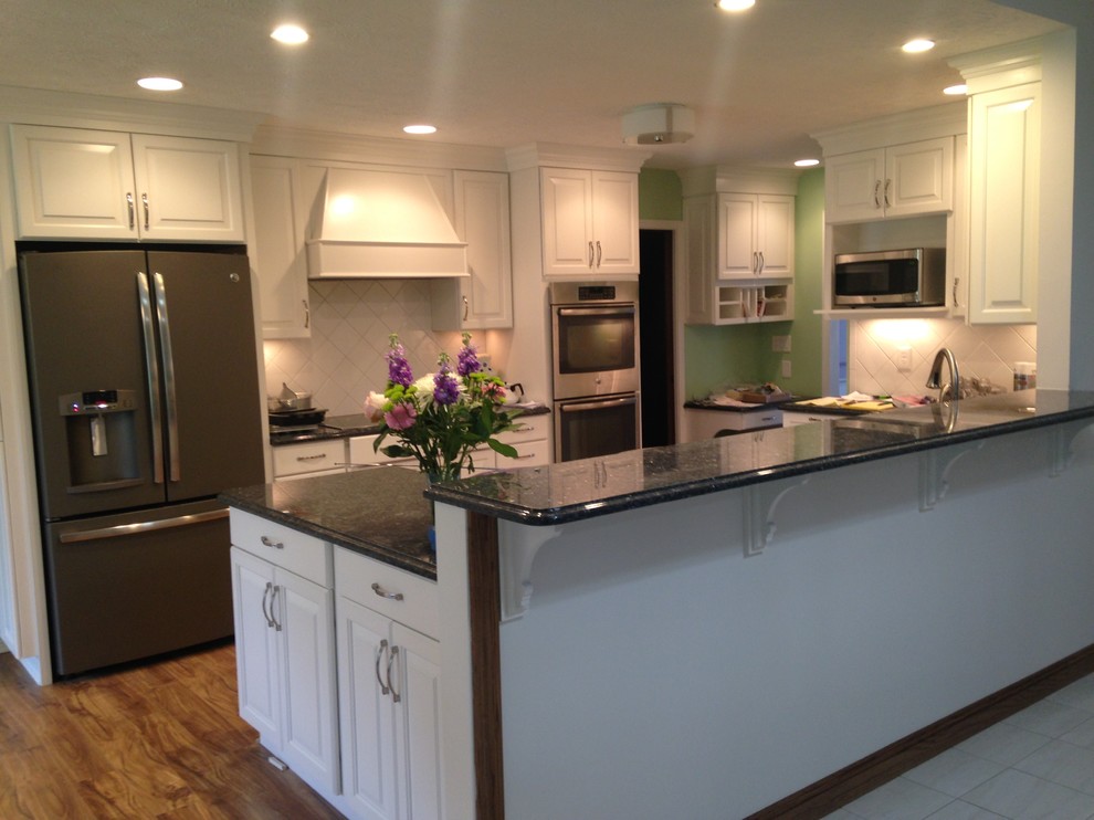 Inspiration for a mid-sized timeless galley medium tone wood floor eat-in kitchen remodel in Cleveland with beaded inset cabinets, white cabinets, granite countertops, white backsplash, cement tile backsplash, stainless steel appliances and an island