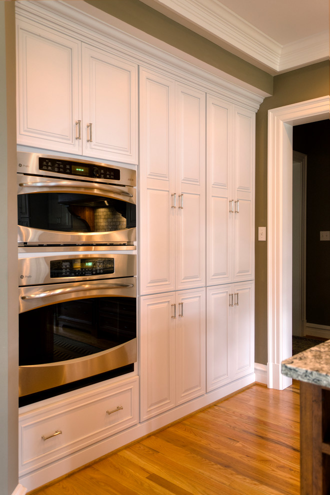 Klassisk inredning av ett kök, med luckor med upphöjd panel, vita skåp, rostfria vitvaror, ljust trägolv och en köksö
