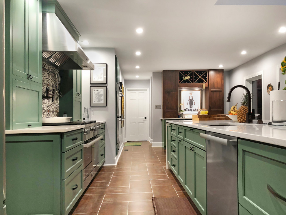 Photo of a large contemporary galley kitchen/diner in DC Metro with a belfast sink, recessed-panel cabinets, green cabinets, engineered stone countertops, multi-coloured splashback, ceramic splashback, stainless steel appliances, ceramic flooring, an island, brown floors and white worktops.