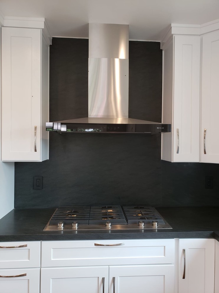Example of a mid-sized trendy l-shaped medium tone wood floor and brown floor enclosed kitchen design in Los Angeles with an undermount sink, shaker cabinets, white cabinets, soapstone countertops, black backsplash, stone slab backsplash, stainless steel appliances, an island and black countertops