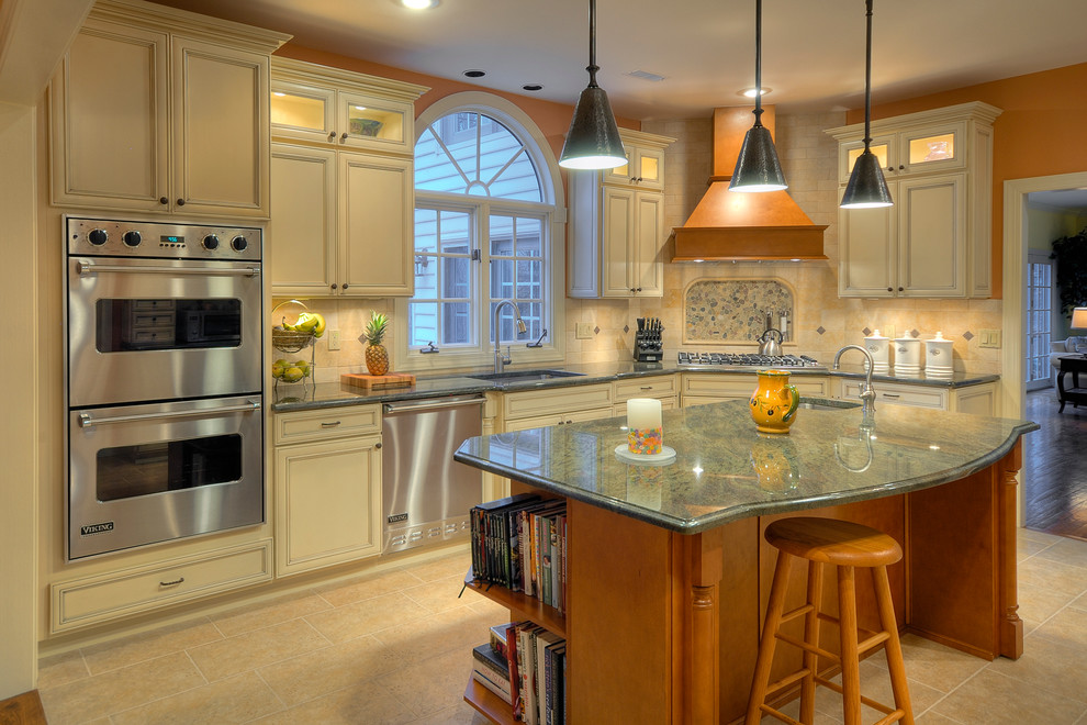 Photo of a large traditional l-shaped kitchen/diner in Philadelphia with granite worktops, a submerged sink, raised-panel cabinets, white cabinets, beige splashback, porcelain splashback, stainless steel appliances, porcelain flooring, an island and green worktops.