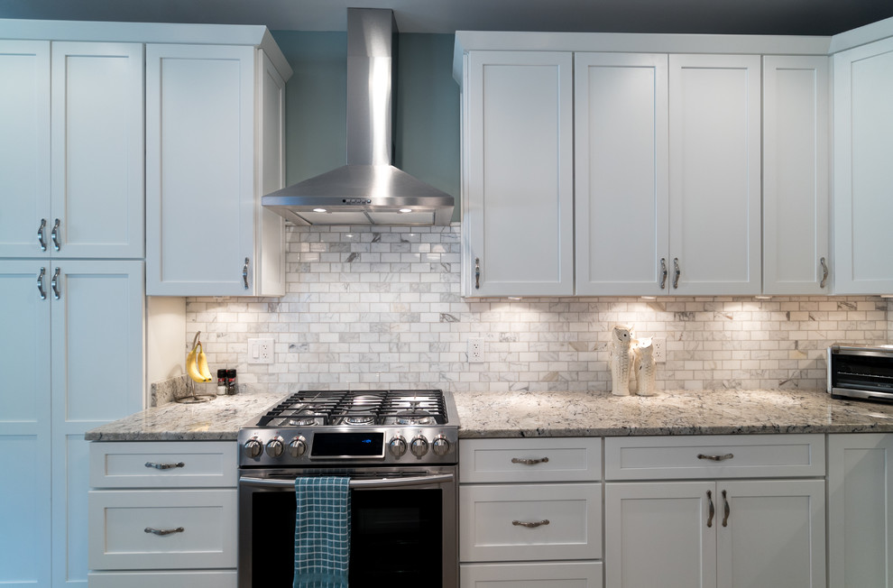 Mid-sized trendy l-shaped kitchen photo in DC Metro with an undermount sink, recessed-panel cabinets, white cabinets, granite countertops, beige backsplash, stone tile backsplash, stainless steel appliances and an island