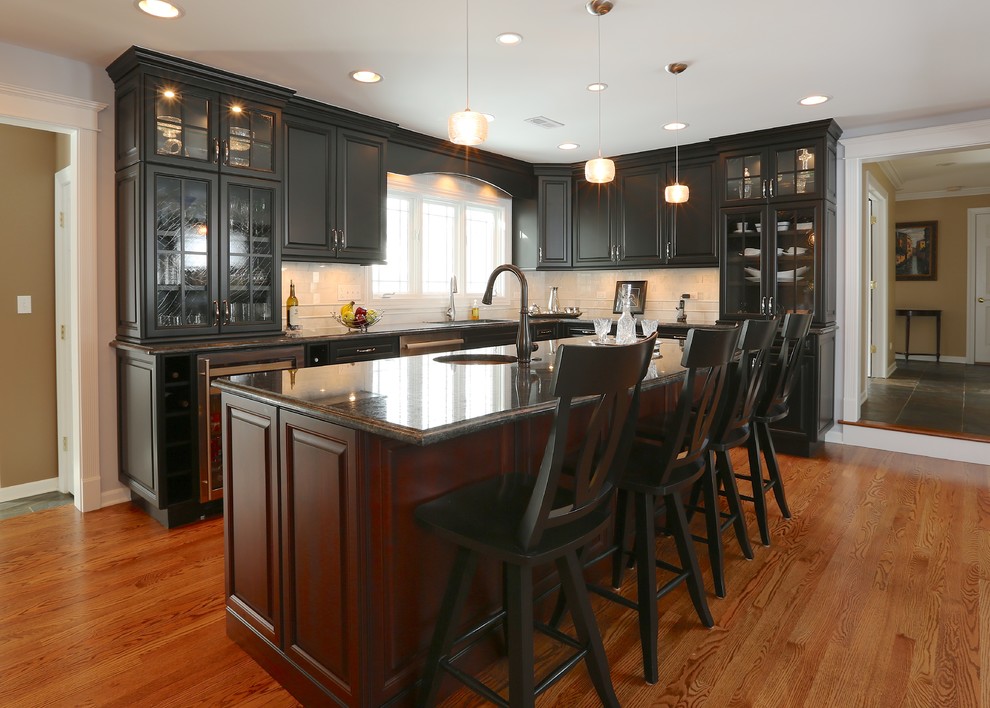 Kitchen - large traditional u-shaped medium tone wood floor kitchen idea in Chicago with a drop-in sink, glass-front cabinets, black cabinets, beige backsplash, stainless steel appliances and an island