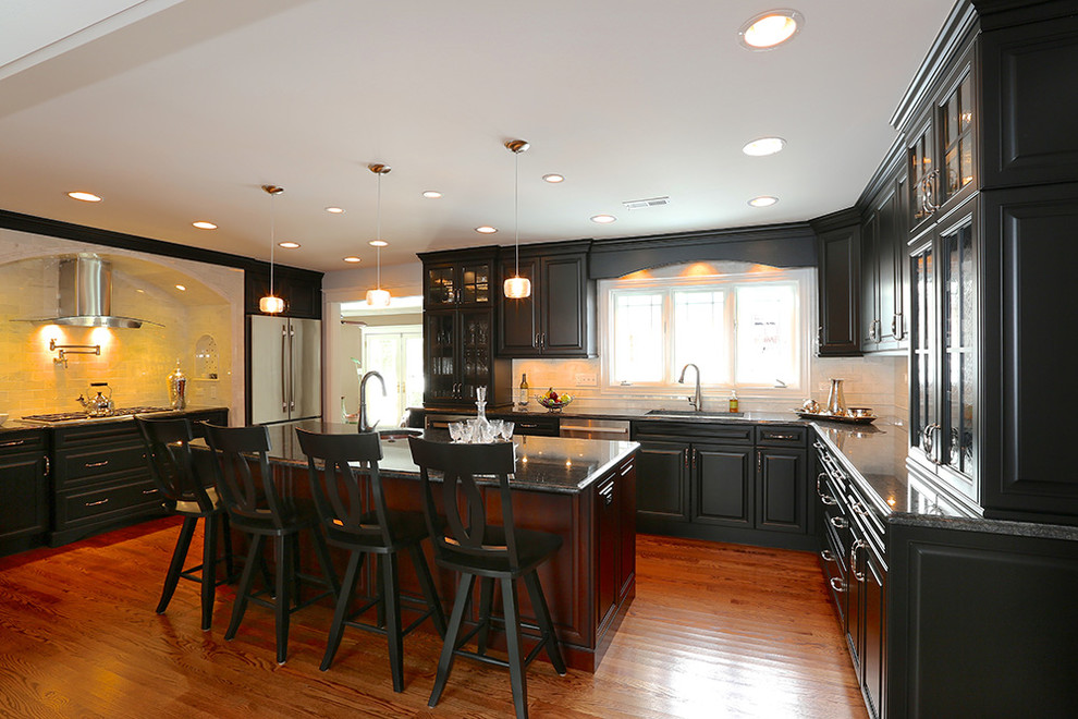 Immagine di una grande cucina chic con lavello da incasso, ante di vetro, ante nere, paraspruzzi beige, elettrodomestici in acciaio inossidabile e pavimento in legno massello medio
