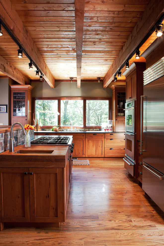 Inredning av ett rustikt brun brunt u-kök, med en undermonterad diskho, skåp i shakerstil, skåp i mellenmörkt trä, träbänkskiva, grått stänkskydd, stänkskydd i mosaik, rostfria vitvaror, mellanmörkt trägolv, en köksö och brunt golv
