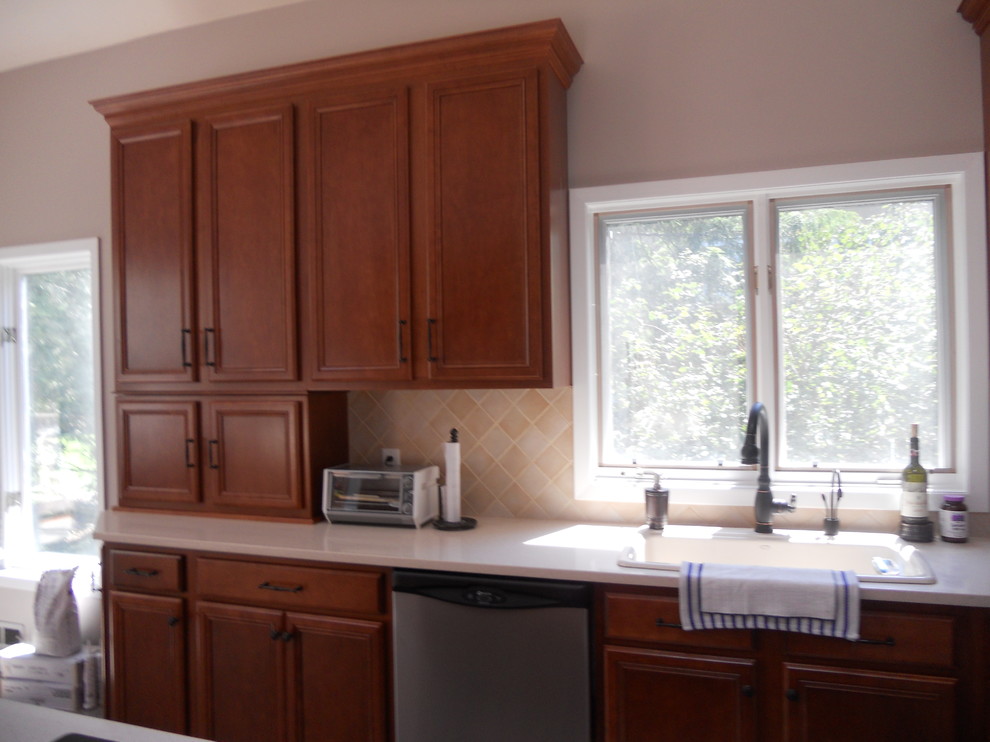 Mid-sized elegant l-shaped eat-in kitchen photo in Newark with a drop-in sink, recessed-panel cabinets, dark wood cabinets, solid surface countertops, beige backsplash, ceramic backsplash, stainless steel appliances and an island