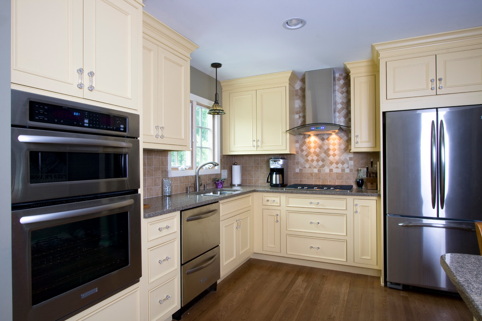 Klassisk inredning av ett mellanstort kök, med en undermonterad diskho, luckor med infälld panel, gula skåp, granitbänkskiva, beige stänkskydd, stänkskydd i keramik, rostfria vitvaror, mellanmörkt trägolv och en köksö