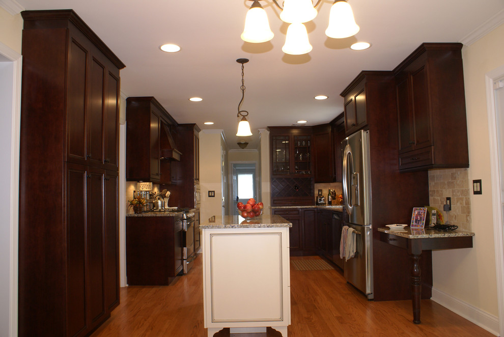 Exempel på ett avskilt, mellanstort klassiskt l-kök, med luckor med infälld panel, skåp i mörkt trä, granitbänkskiva, rostfria vitvaror, mörkt trägolv och en köksö
