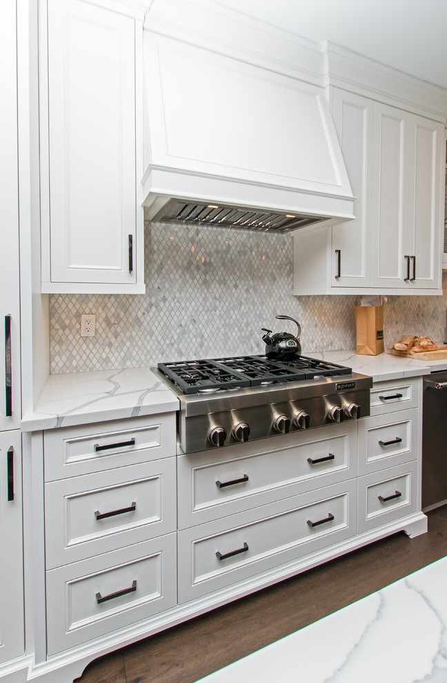 Bild på ett avskilt, stort vintage vit vitt l-kök, med en undermonterad diskho, luckor med infälld panel, vita skåp, marmorbänkskiva, grått stänkskydd, stänkskydd i mosaik, rostfria vitvaror, mellanmörkt trägolv, en köksö och brunt golv
