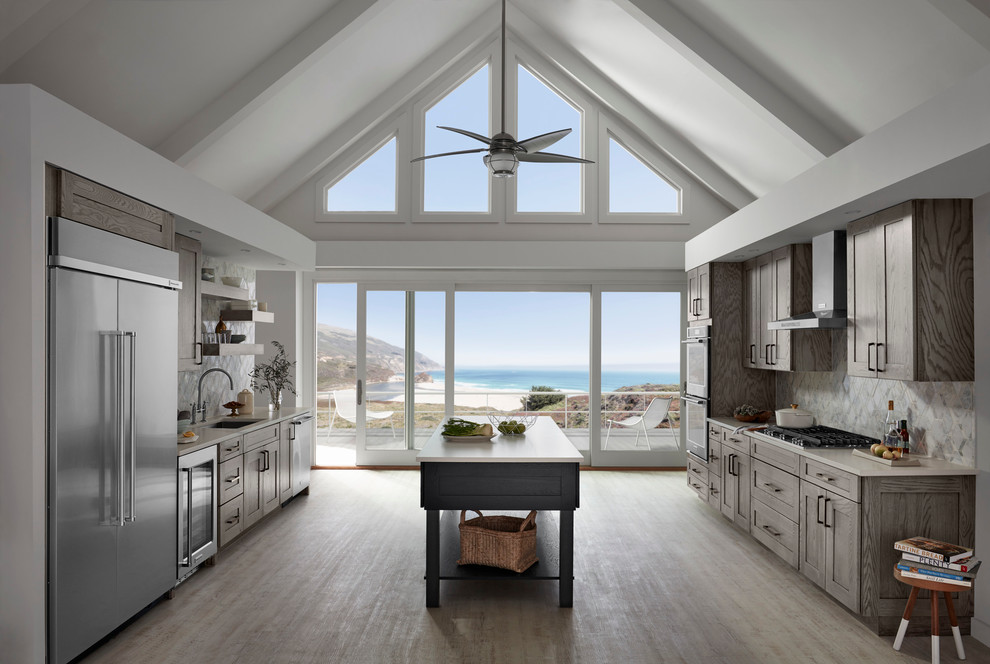 This is an example of a large coastal u-shaped kitchen/diner in Other with a submerged sink, shaker cabinets, light wood cabinets, engineered stone countertops, multi-coloured splashback, stainless steel appliances, light hardwood flooring, an island and brown floors.