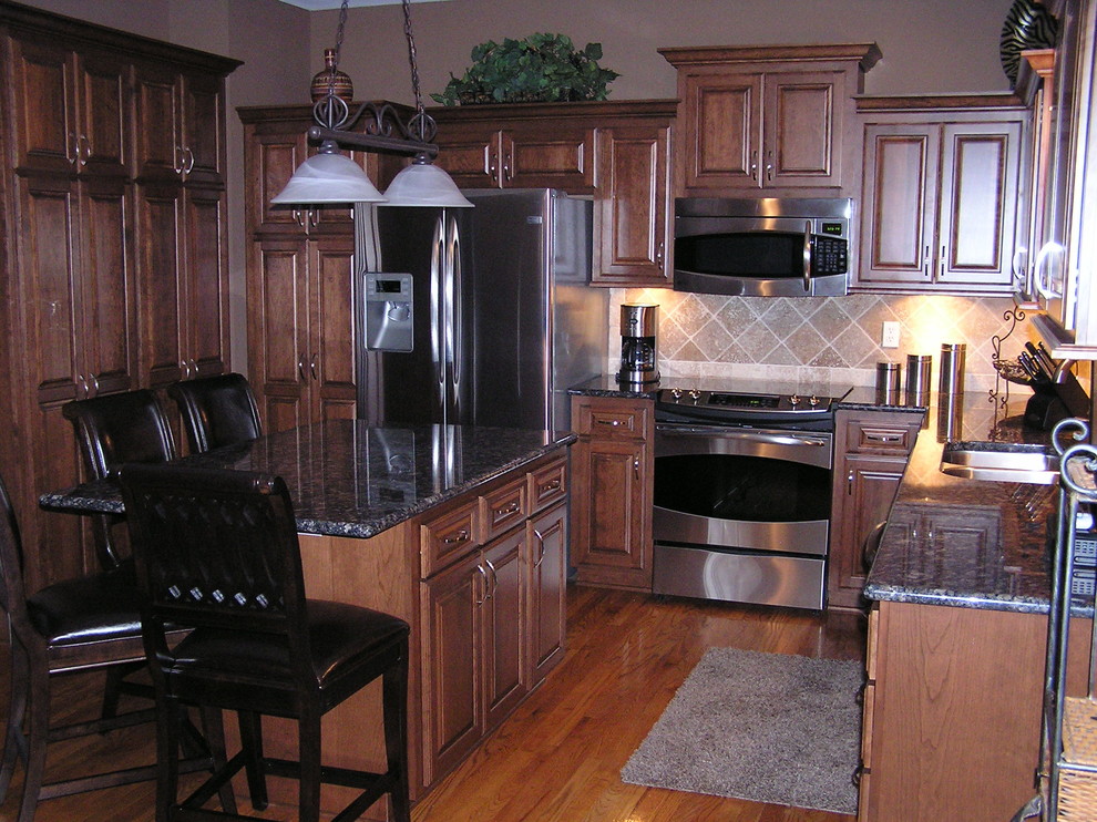 Eat-in kitchen - large traditional u-shaped medium tone wood floor and brown floor eat-in kitchen idea in Kansas City with raised-panel cabinets, medium tone wood cabinets, granite countertops, beige backsplash, ceramic backsplash, stainless steel appliances, an island and a double-bowl sink