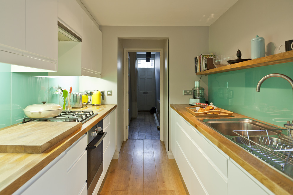 Cette photo montre une cuisine parallèle rétro fermée avec un plan de travail en bois, un évier posé, un placard à porte plane, des portes de placard blanches et une crédence en feuille de verre.