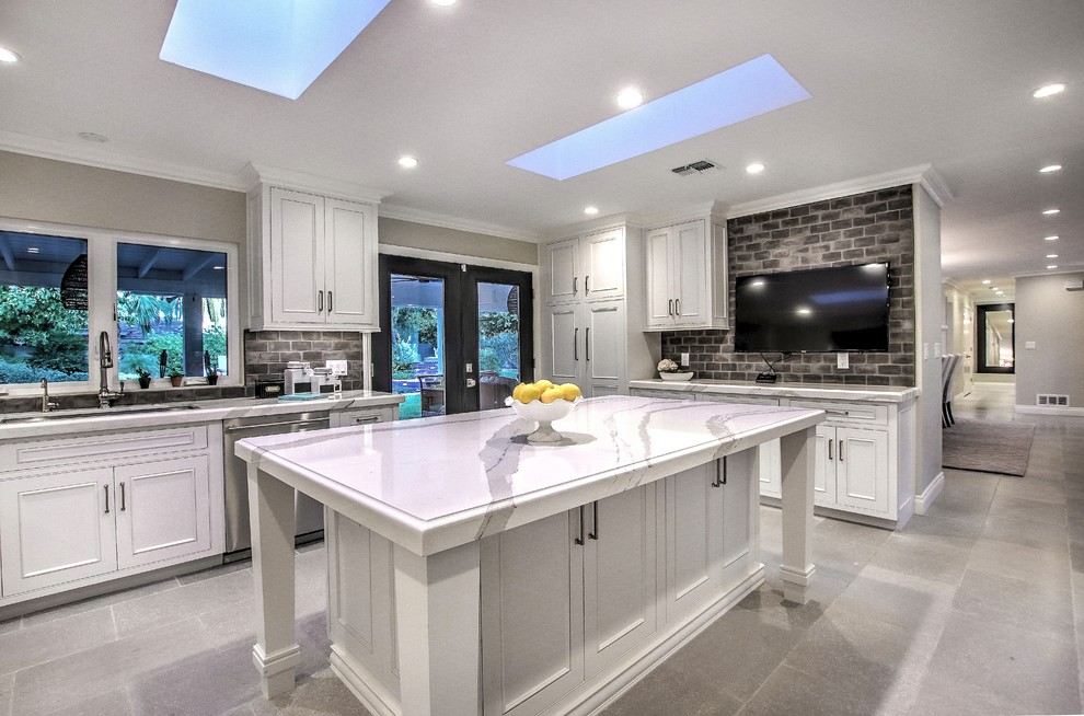 Inspiration for a classic grey and white kitchen in Phoenix with raised-panel cabinets, white cabinets, grey splashback, brick splashback, stainless steel appliances, an island and grey floors.