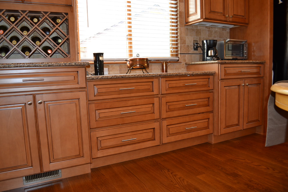 Klassisk inredning av ett mellanstort kök, med en undermonterad diskho, luckor med upphöjd panel, skåp i mellenmörkt trä, bänkskiva i kvarts, beige stänkskydd, stänkskydd i stenkakel, svarta vitvaror och mellanmörkt trägolv
