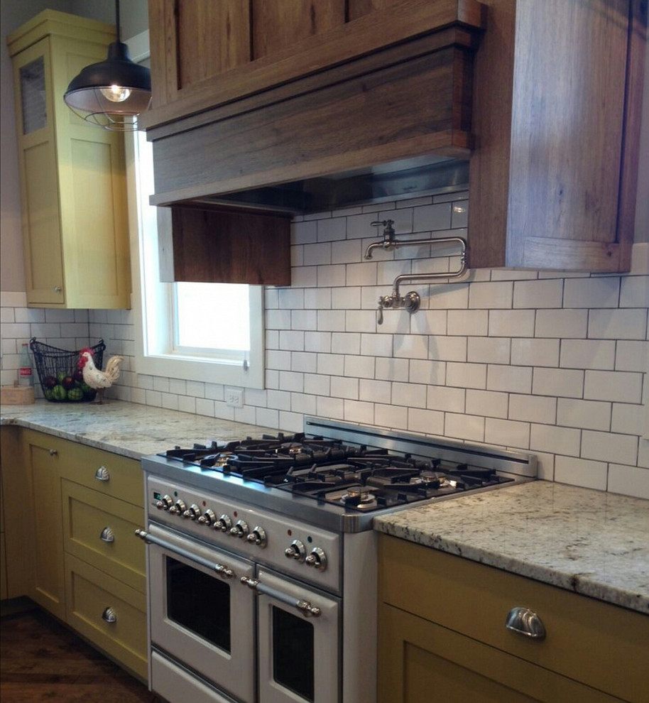 Bild på ett mellanstort lantligt grå grått kök, med skåp i shakerstil, gula skåp, granitbänkskiva, vitt stänkskydd, stänkskydd i tunnelbanekakel, vita vitvaror, mellanmörkt trägolv och brunt golv