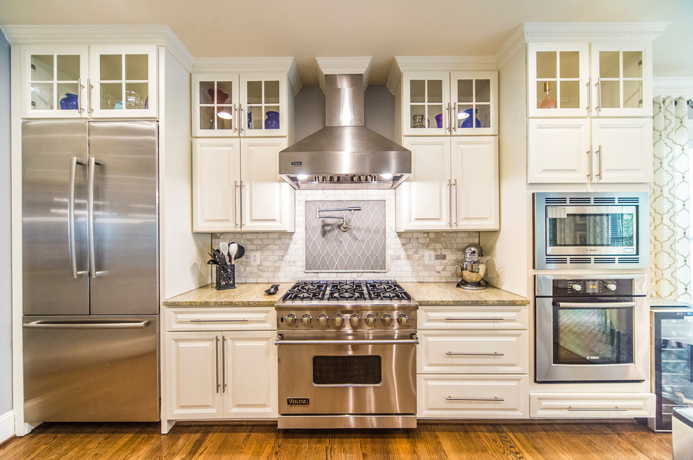 Example of a mid-sized classic l-shaped medium tone wood floor and beige floor eat-in kitchen design in DC Metro with a single-bowl sink, recessed-panel cabinets, white cabinets, granite countertops, beige backsplash, stone tile backsplash, stainless steel appliances and a peninsula