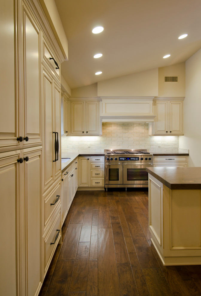 Imagen de cocinas en L de estilo americano con puertas de armario de madera clara, salpicadero blanco y electrodomésticos de acero inoxidable