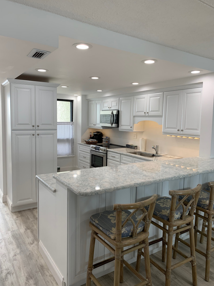 Small traditional l-shaped kitchen/diner in Philadelphia with a submerged sink, raised-panel cabinets, white cabinets, granite worktops, stainless steel appliances, laminate floors, a breakfast bar, grey floors and grey worktops.
