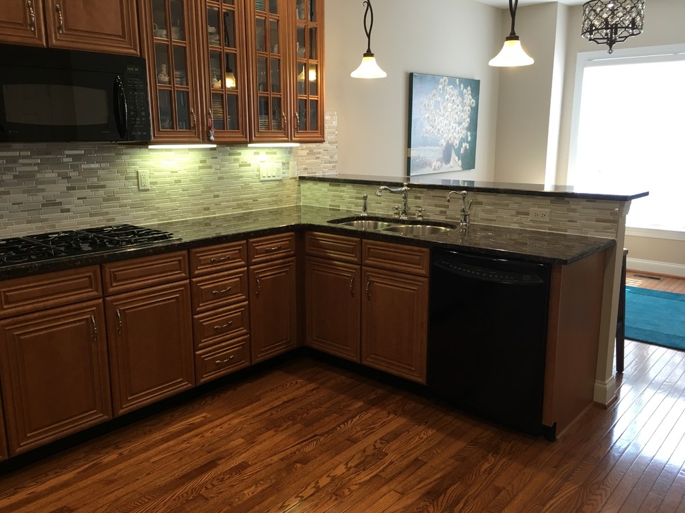 Inredning av ett klassiskt mellanstort kök, med en dubbel diskho, luckor med upphöjd panel, granitbänkskiva, grått stänkskydd, stänkskydd i stickkakel, svarta vitvaror, plywoodgolv, en halv köksö, skåp i mellenmörkt trä och brunt golv