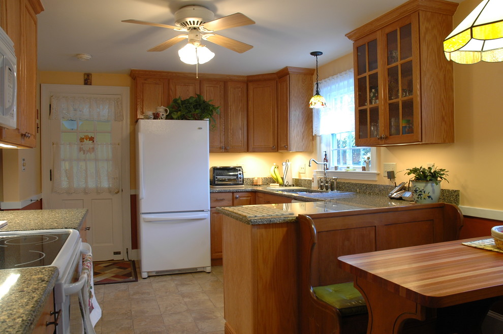 Inredning av ett lantligt litet kök, med en undermonterad diskho, luckor med upphöjd panel, skåp i mellenmörkt trä, granitbänkskiva, flerfärgad stänkskydd, vita vitvaror, linoleumgolv och en halv köksö