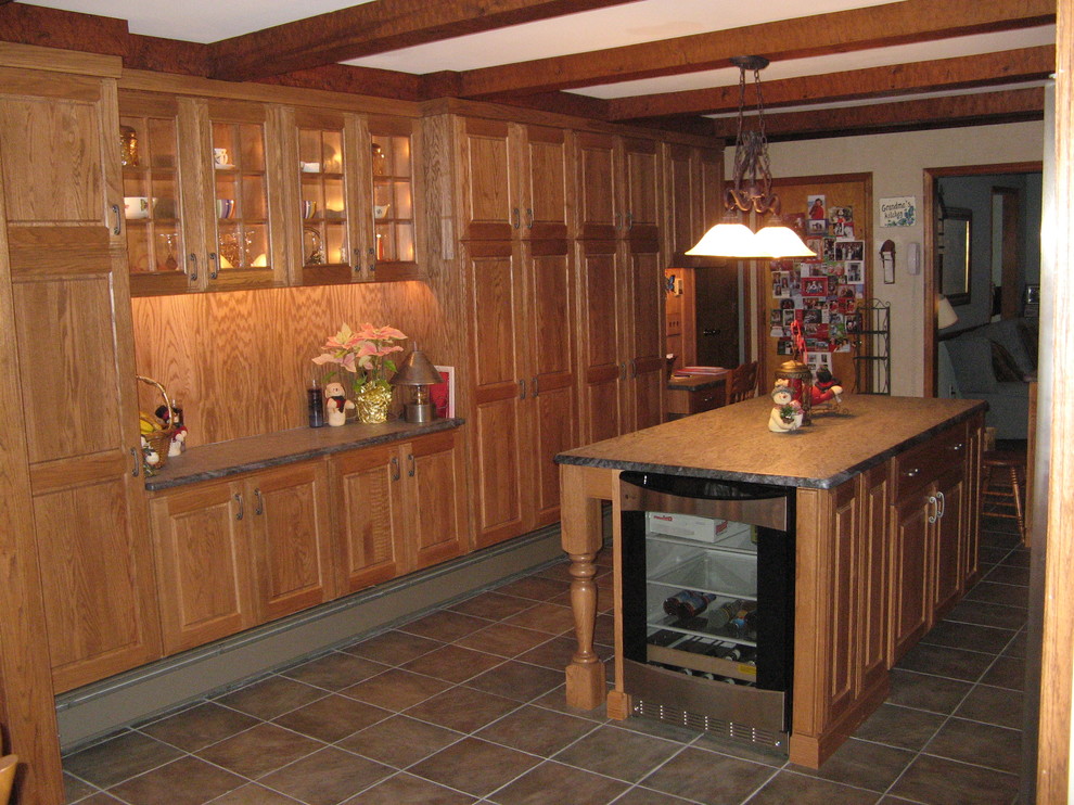 L-shaped kitchen/diner in New York with a built-in sink, raised-panel cabinets, medium wood cabinets, granite worktops, stainless steel appliances, cement flooring, an island and brown floors.